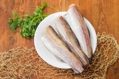 Alaska pollock 'unun çözülmemiş cesetleri taze maydanozlu ve balık ağının bir parçasıyla eski bir kırsal masada, üst manzaralı.
