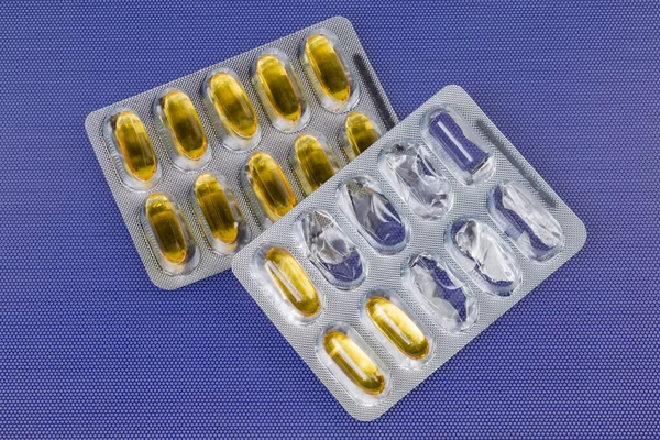 Pharmaceutical drugs in the form of yellow translucent gelatin capsules in one started and in one whole blister packing on a blue surface, top view