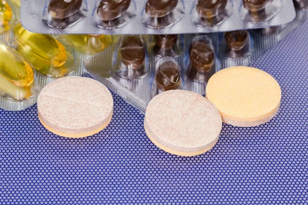 Effervescent tablets against the yellow and brown capsules in different blister packing on a blue surface, close-up in selective focu