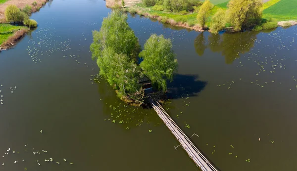 彼に木や木の歩道橋の間に小屋と湖の上の小さな島 春の空中風景 — ストック写真