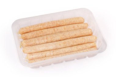 Pişmemiş uzun tavuk sosisleri beyaz arka planda şeffaf plastik konteynır şeklinde paketleniyor.