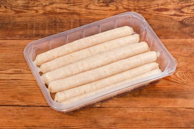 Pişmemiş uzun tavuk sosisleri kırsal bir masada şeffaf plastik konteynır şeklinde paketlenir.