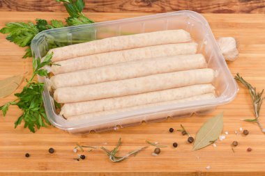Pişmemiş uzun tavuk sosisleri baharatlar arasında şeffaf plastik bir kap şeklinde paketlenir.