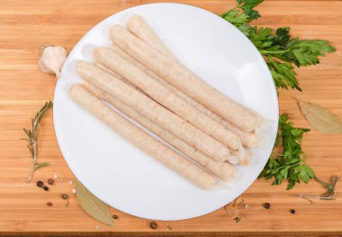 Tabakta çiğ, uzun tavuk sosisi, ahşap kesim tahtası, baharatlar arasında, üst manzara.