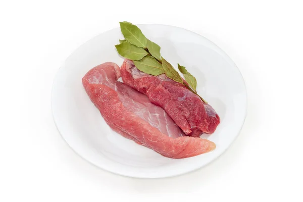 冷却された調理されていない赤身の豚肉 白い背景に白い皿の上に乾燥した湾の葉の小枝 — ストック写真