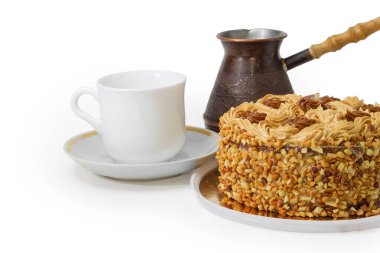 Yuvarlak sünger kek, tereyağı kreması ve karamelize edilmiş süt ile süslenmiş, rendelenmiş fındık serpiştirilmiş küçük beyaz fincana ve klasik bakır kahve demliğine serpiştirilmiş, beyaz arka planda bir parça.