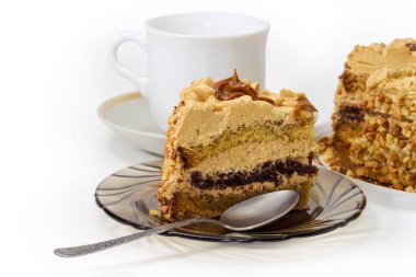 Katmanlı sünger keki, tereyağlı krema, karamelize edilmiş süt, fındık ezilmiş fındıklar beyaz fincanda kaşıkla, beyaz arka planda.