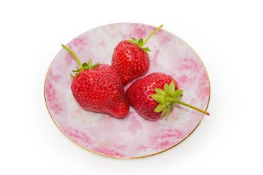 Beyaz arka planda pembe bir fincan tabağında kuyrukları olan taze olgun çilekler.