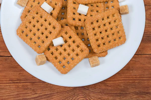 フラットカリカリ正方形型の砂糖ショートブレッドクッキーと古い素朴なテーブルの上に白い皿の白と茶色の砂糖キューブ フラグメントトップビュー — ストック写真