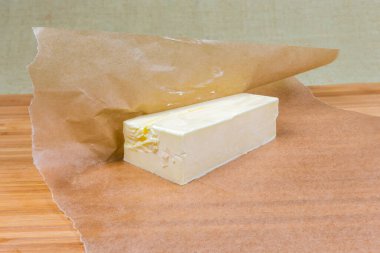 Ağda kağıdına sarılı katı tereyağı parçası ahşap bir yüzey üzerinde yatıyor.