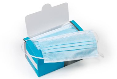 Açık mavi tek kullanımlık tıbbi yüz maskesi beyaz arka plandaki aynı maskelerin açık karton ambalajında bulunur.