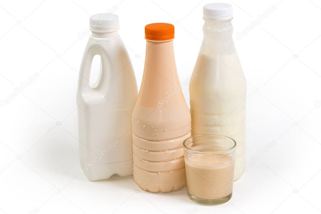 Fermented baked milk in glass against the plastic bottles of various dairy products on a white background, side view 