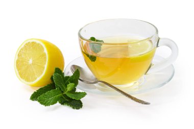 Bir bardak nane yaprağı ve limon dilimli çay çay fincanı çay kaşıklı çay tabağı, taze nane dalı ve beyaz arka planda yarım limon.