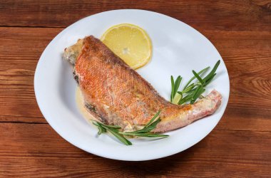 Okyanus levreği eski bir kırsal masada beyaz tabakta ekşi krema sosunda pişirilmiş.