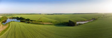 Yaz akşamları göletli vadinin hafif yamaçlarında yeşil olgunlaşmamış buğday tarlaları, havadan panoramik manzara