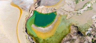 Ormana karşı terk edilmiş ilmenit taş ocağının olduğu yerde, dikey hava manzaralı eski atık kaya çöplüklerinin arasında renkli bir göl oluştu.