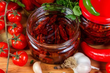 Kurutulmuş domatesler bitkisel yağda korunmuş, bitkiler küçük kavanozda, malzemeler arasında, seçici odak noktasında yakın plan.