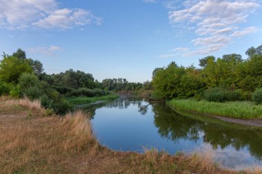 Sakin, sade nehrin ağaçlar, çalılar ve çimlerle kaplanmış kıyıları yaz sabahları.
