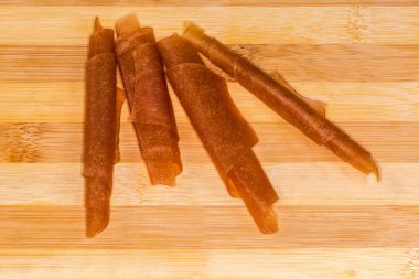 Kurutulmuş kayısı püresinden yapılmış ince, yumuşak, esnek kayısı pastila ahşap bambu kesme tahtasındaki borulara sarılmış, yakın çekim.