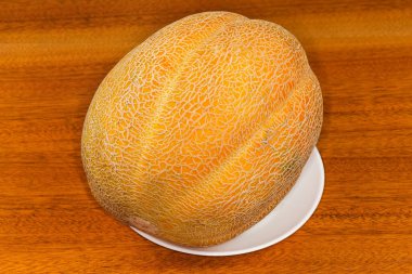 Whole fresh melon with yellow netted skin on white dish on a wooden table