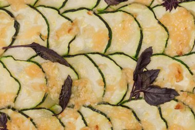 Surface of cooked casserole with zucchini and cheese on the dough base, or so-called zucchini pizza decorated with purple basil leaves on baking sheet, fragment top view close-up