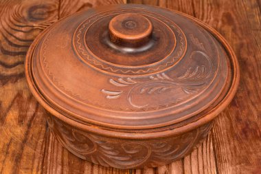Yuvarlak kavruk, kapalı kapaklı, doğal kırmızı kilden yapılmış ve kırsal bir masa üzerindeki çiçek süsüsüyle süslenmiş.