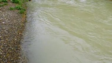 Dağ nehrinde çamurlu su akışı, yaya köprüsünden manzara