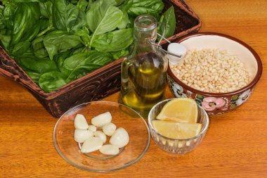 Ahşap bir masada fesleğen sosu hazırlamak için ezilen ve rendelenmiş peynire eklenen ham malzemeler.