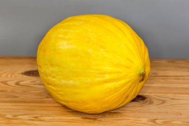 Gri arka planda, ahşap bir kırsal masa üzerinde parlak sarı ciltli taze kavun.