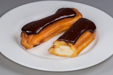 Beyaz bir tabakta krema ve çikolata kaplı bir tam ve bir yarım eklem, seçici odak noktasında ön plan.