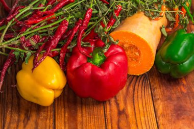 Üç dolmalık biber, farklı renkler ve yarım balkabağı ve kuru kırmızı biber eski ahşap bir masa üzerinde solmuş sapı, parçalanmış üst görünüm.