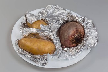 Az sayıda patates ve bir kırmızı pancar yemek folyosuna sarılı olarak gri bir arka planda beyaz bir tabakta yatıyor.