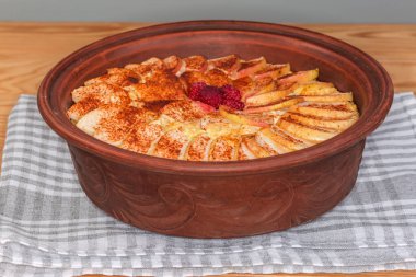 Elma dilimleri katmanı ve ahududu ile pişirilmiş, ahşap bir masa üzerinde peçete üzerine toprak kavrulmuş tarçın serpiştirilmiş, seçici bir odak noktasında ön görüş olan süzme peynir güveci.