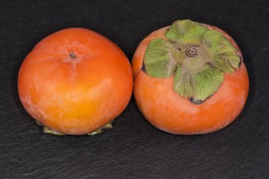 Siyah düz tabakta iki olgun taze, yuvarlak hurma meyvesi Fuyu çeşidi.