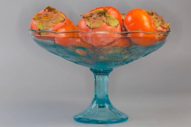 Taze, taze, yuvarlak hurma ağaçları. Fuyu çeşidi. Gri arka plandaki mavi cam meyve kasesinde.