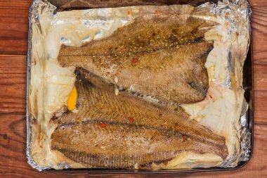 İki dil balığı, aynı zamanda bembeyaz olarak da bilinir, metal pişirme tepsisinde soğan ve baharatla pişirilmiş, folyoyla kaplanmış, yakın plan.
