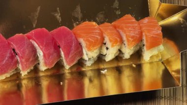 Suşi, somon balıklı uramaki ve altın ambalajlı ton balığı sarıyor.