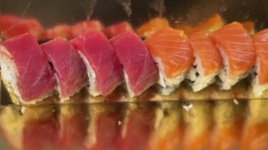 Suşi, somon balıklı uramaki ve altın ambalajlı ton balığı sarıyor.