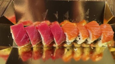 Suşi, somon balıklı uramaki ve altın ambalajlı ton balığı sarıyor.