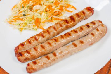 Izgara ızgara, uzun domuz sosisi ve beyaz tabakta sebze salatası.