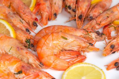 Kabuksuz kral karidesleri kaynatılmış yeşillerle kaynatılmış beyaz tabakta taze limon dilimleri serilmiş, seçici odak noktasında parçalanmış.