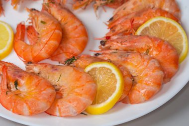 Beyaz tabakta taze limon dilimleri olan taze haşlanmamış kral karidesleri, seçici bir odak noktası olan parça.