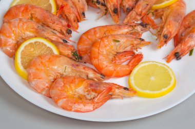 Kabuksuz kral karidesler yeşillerle kaynatılmış, beyaz tabakta taze limon dilimleri serilmiş, seçici odak noktasında parçalanmış.