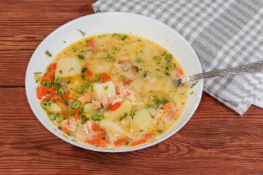 Somon, karides, midye ve sebzeli sıcak kremalı çorba. Beyaz tabakta kaşık ve peçeteli kırsal bir masada.