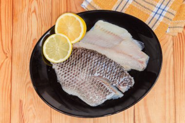 İki buzu çözülmüş çiğ dourade fileto kemiksiz balık leşi şeklinde derisi üzerinde taze limon parçacıklarıyla kırsal bir masada, üst görünümde.