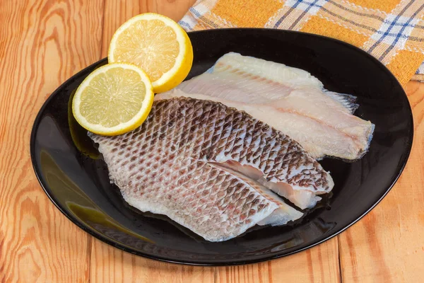 İki buzu çözülmüş çiğ İspanyol fileto kemiksiz balık leşi şeklinde derisi üzerinde taze limon parçaları kırsal bir masada siyah bir tabakta.