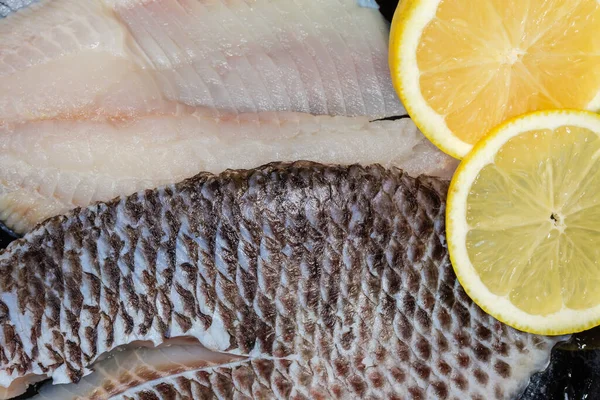 Taze limon parçalarının olduğu deride kemiksiz balık leşi şeklinde çözülmüş iki çiğ dourade fileto, yakın çekim parçasının üst görüntüsü.