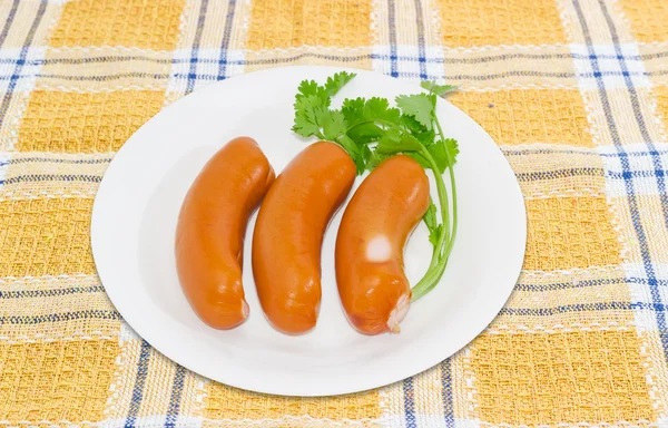 Three uncooked bangers in natural casing and branch of coriander — Stock Photo, Image