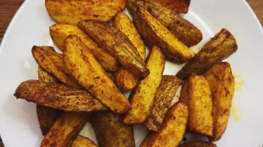 Beyaz tabakta baharatlı fırında patates dilimleri.