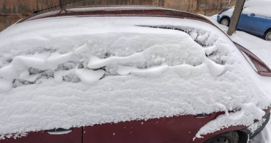 Kar yağışı kışın bulutlu geçen kar fırtınasından sonra park halindeki kırmızı bir arabanın yan ve arka tarafına yerleşmiş.